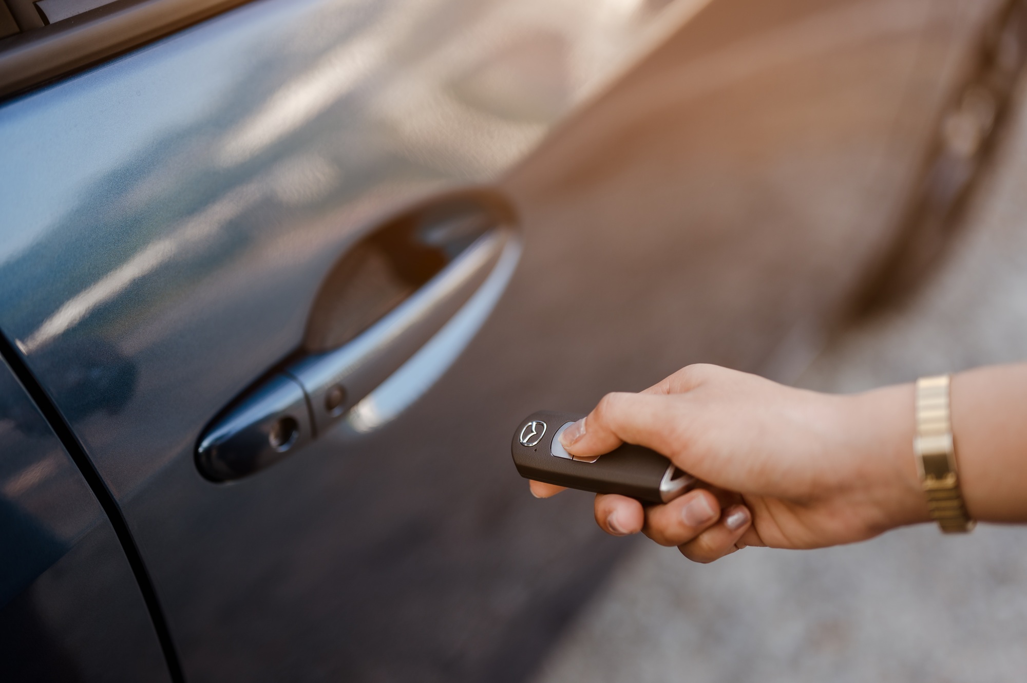 Close up hands woman pressing remote systems key near car for unlock of blue car near street
